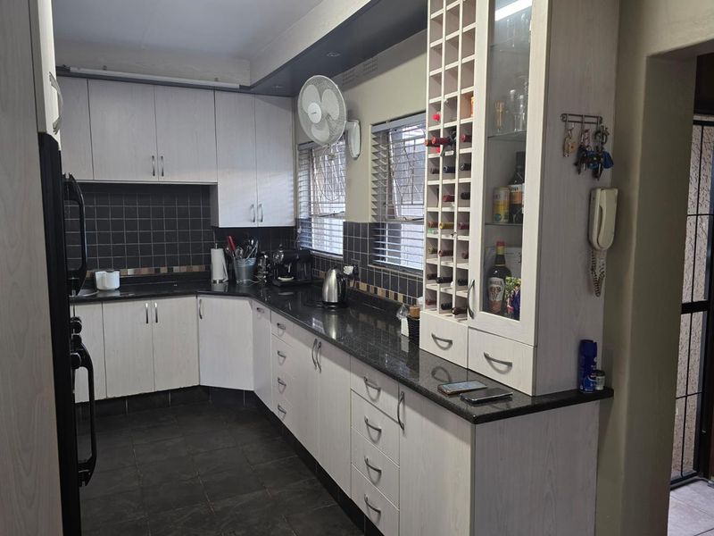 A functional kitchen featuring light-toned cabinetry, dark granite countertops, a built-in wine rack, and a tiled backsplash.