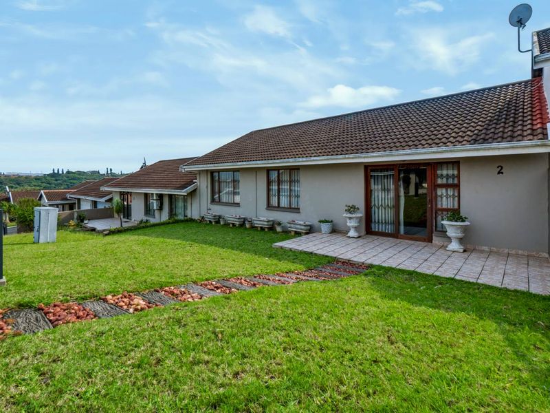 Rear view of the townhouse featuring a tiled patio, well-maintained lawn, and sliding glass door access.