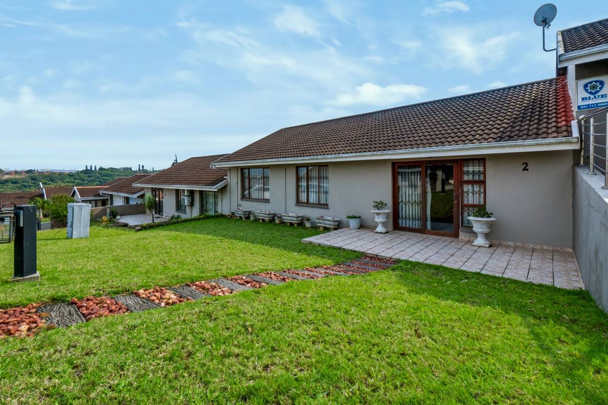 Rear view of the townhouse featuring a tiled patio, well-maintained lawn, and sliding glass door access.