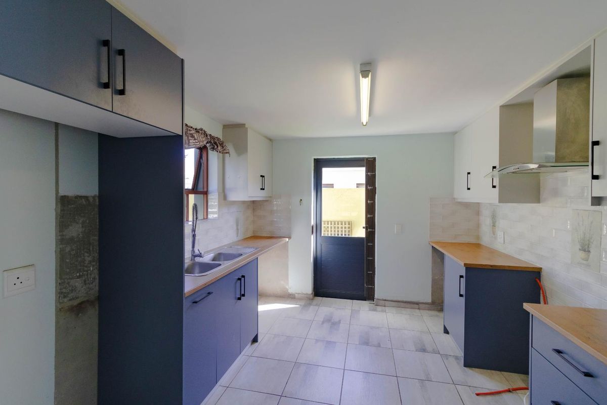 A functional kitchen featuring modern blue and white cabinetry, wooden countertops, tiled backsplash, and direct access to the exterior.