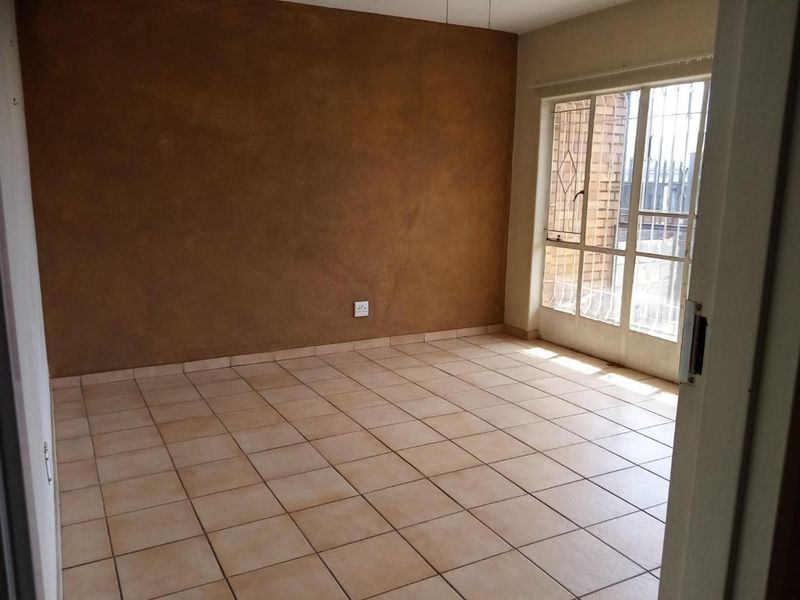 An empty living room featuring ceramic floor tiles, a textured accent wall, and a sliding glass door with an integrated security gate.