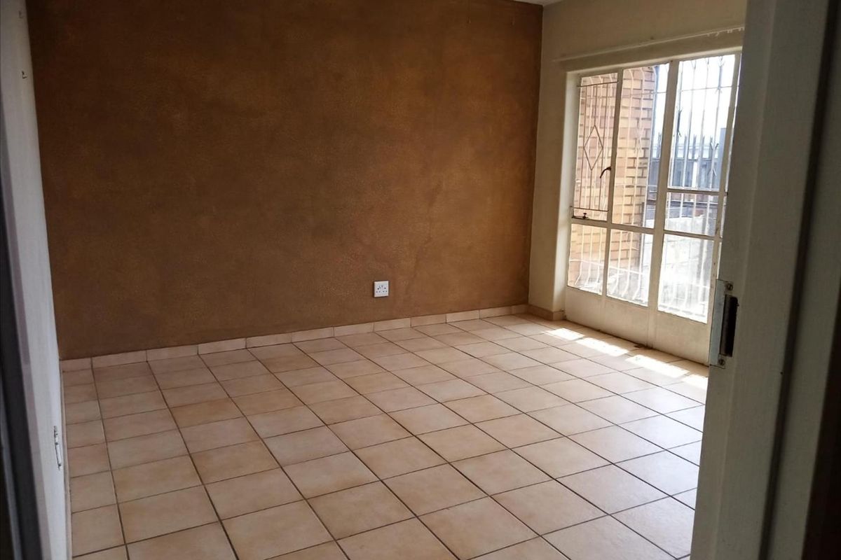 An empty living room featuring ceramic floor tiles, a textured accent wall, and a sliding glass door with an integrated security gate.