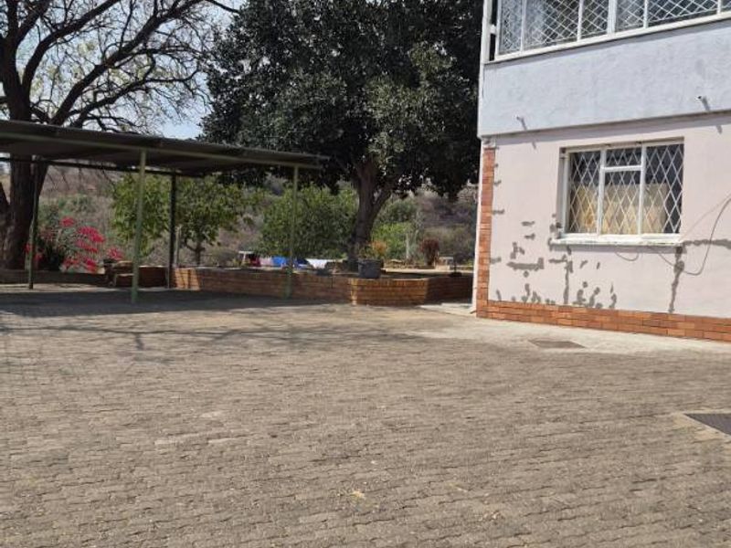 Exterior view of the property featuring a paved driveway, a carport, and a multi-story building with security-barred windows and visible exterior wall maintenance needs.