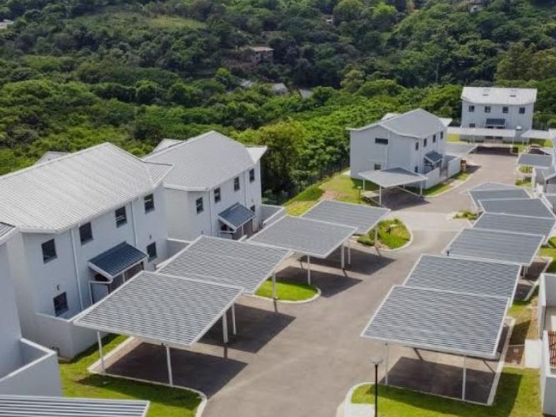 Aerial view of a modern townhouse complex featuring multiple residential units, covered carports, paved driveways, and well-maintained green spaces.