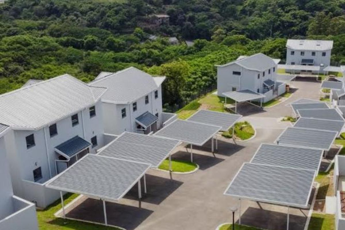 Aerial view of a modern townhouse complex featuring multiple residential units, covered carports, paved driveways, and well-maintained green spaces.