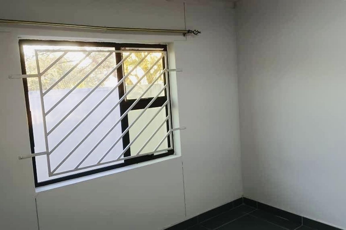 A clean, empty bedroom featuring tiled flooring, a window with security bars, and neutral wall finishes.