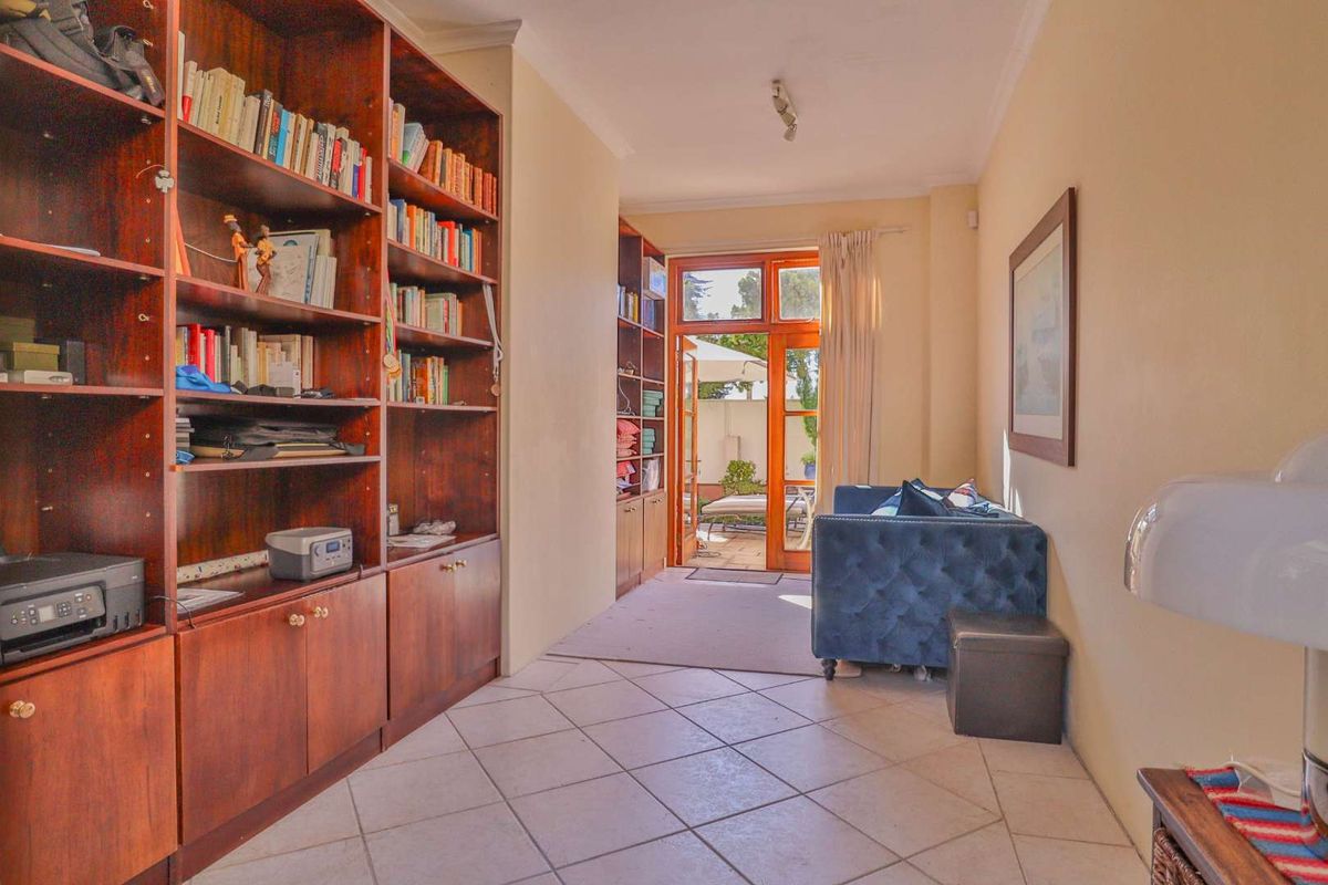 A bright living area featuring built-in wooden shelving units, tiled flooring, and direct access to an outdoor patio through glass-paneled doors.