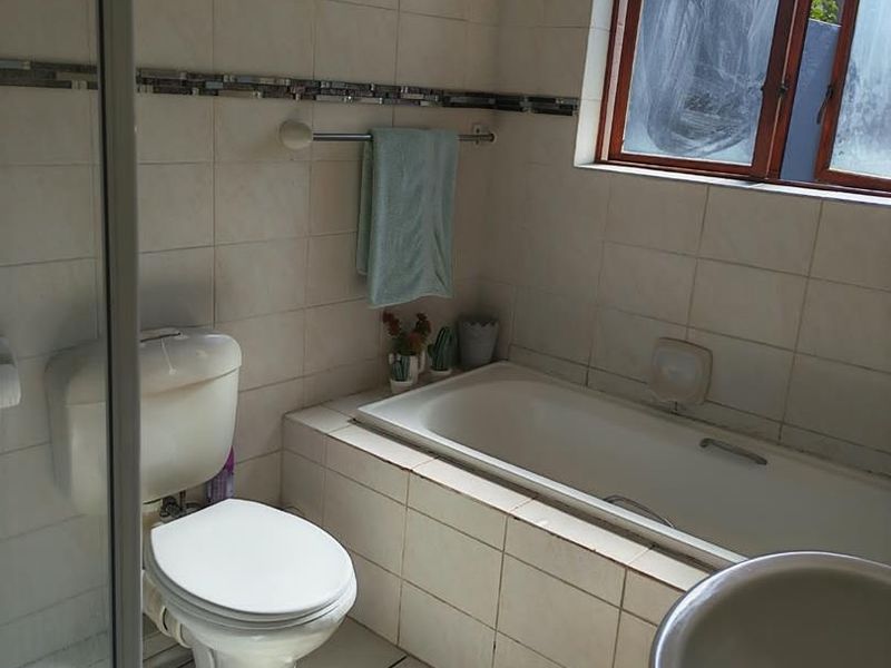 A functional bathroom featuring a built-in bathtub, toilet, shower enclosure, and basin with tiled finishes throughout.
