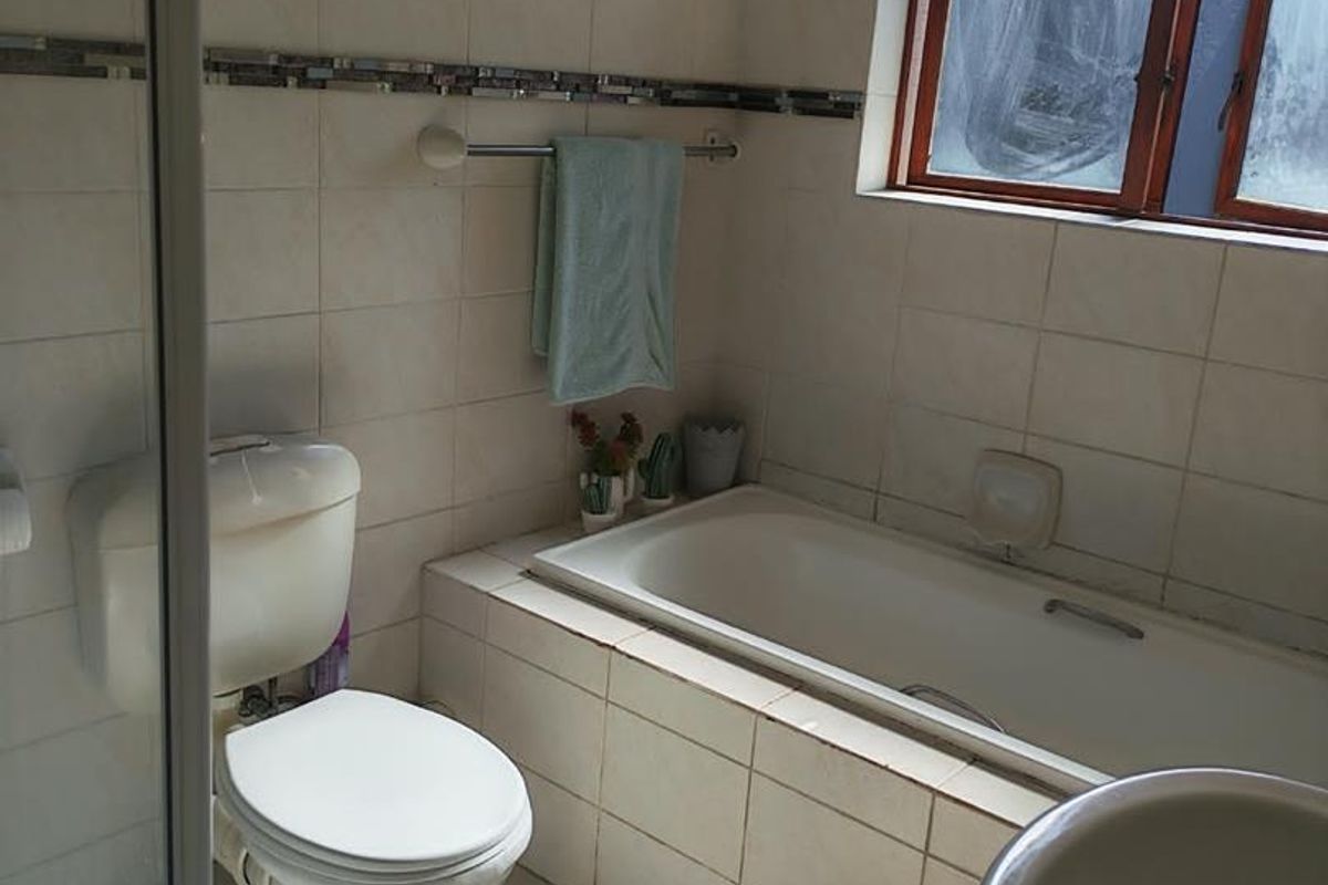 A functional bathroom featuring a built-in bathtub, toilet, shower enclosure, and basin with tiled finishes throughout.