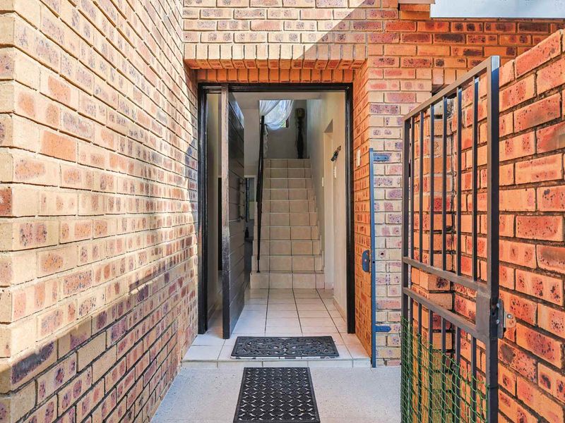 A private entrance area featuring face brick walls, a metal security gate, and tiled flooring leading to an internal staircase.