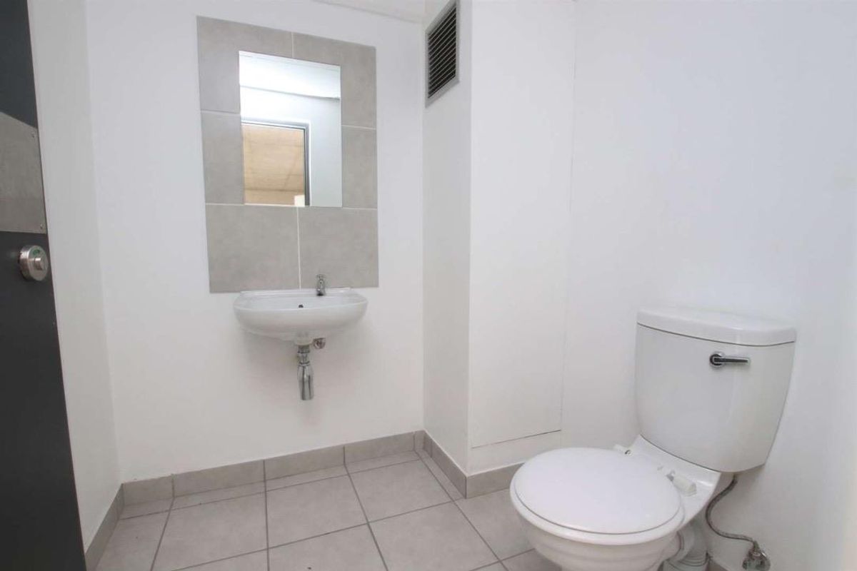 A compact bathroom featuring a wall-mounted basin with a tiled splashback, a mirror, and a standard toilet.
