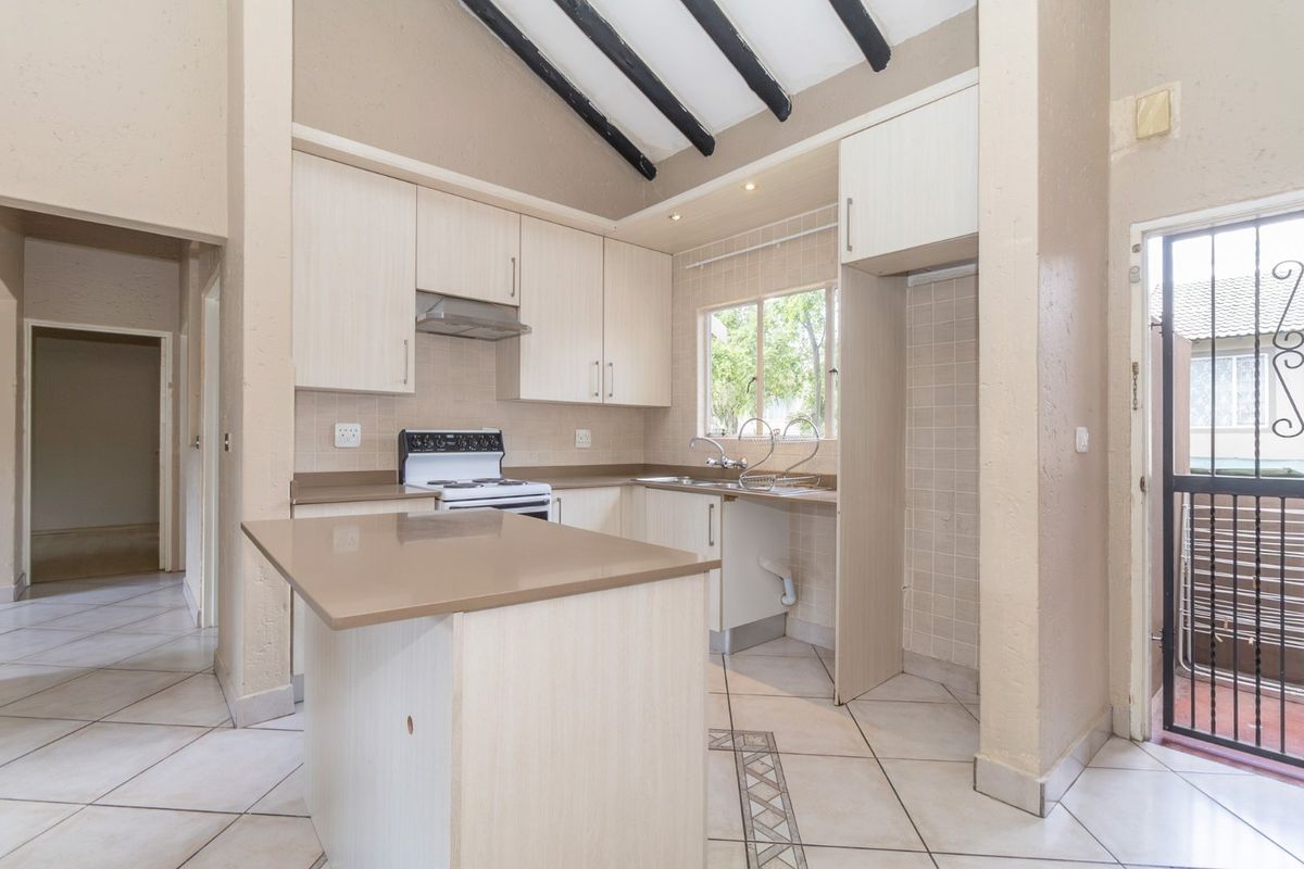 Kitchen featuring light wood cabinetry, stone countertops, exposed ceiling beams, and tiled flooring, with direct access to an exterior area via a security gate.