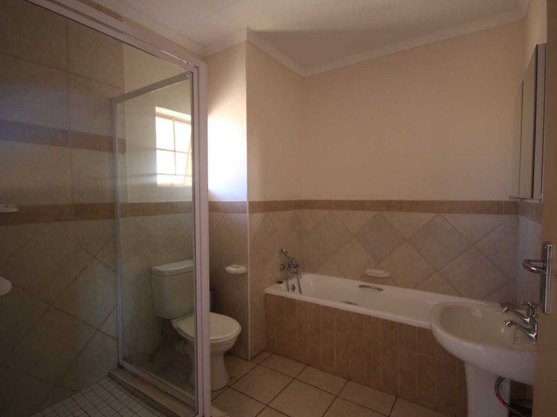 A functional bathroom featuring a separate shower enclosure, bathtub, pedestal basin, and toilet with neutral wall and floor tiling.