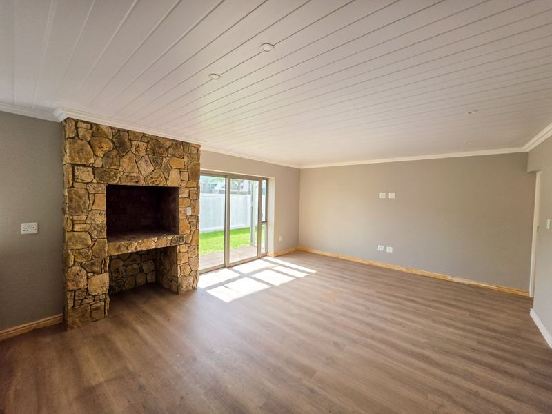 Spacious living room featuring a rustic stone fireplace, wood-look laminate flooring, and sliding glass doors providing direct access to the garden.