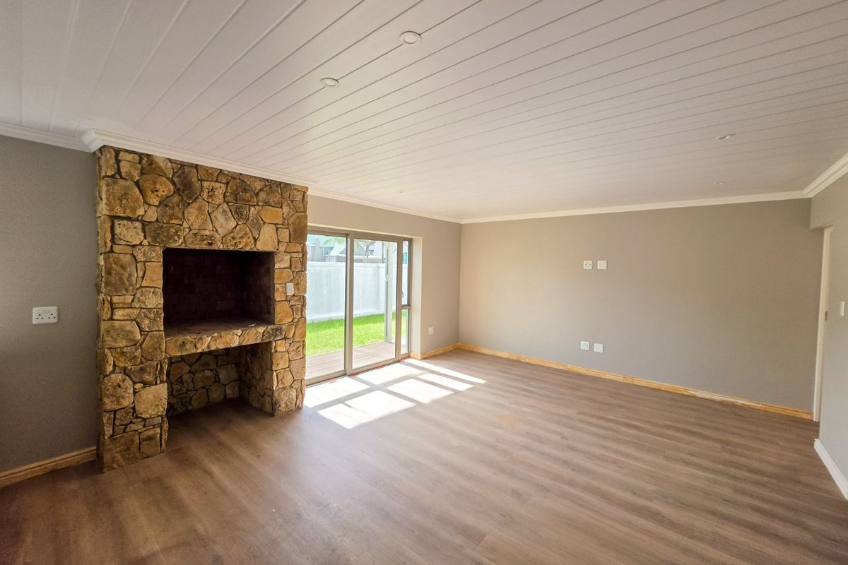 Spacious living room featuring a rustic stone fireplace, wood-look laminate flooring, and sliding glass doors providing direct access to the garden.