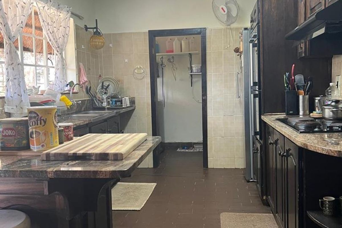 A functional kitchen featuring dark wood cabinetry, granite-style countertops, a built-in hob, and an extractor fan, with an adjacent scullery area.