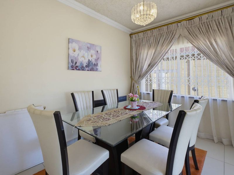 A well-lit dining room featuring tiled flooring, decorative ceiling cornice, and a crystal chandelier, providing a functional space for family meals.