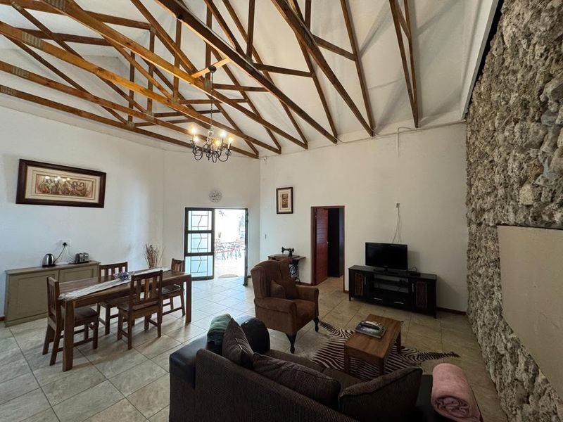 Spacious open-plan living and dining area featuring high vaulted ceilings with exposed timber trusses and a prominent natural stone feature wall.