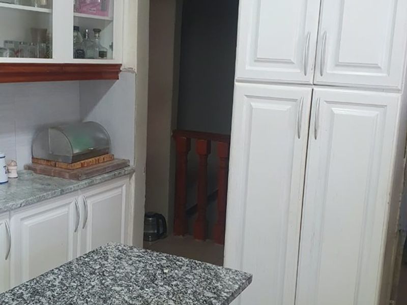 A kitchen area featuring white cabinetry, granite countertops, and a pantry cupboard, with tiled flooring and a view into an adjacent hallway.