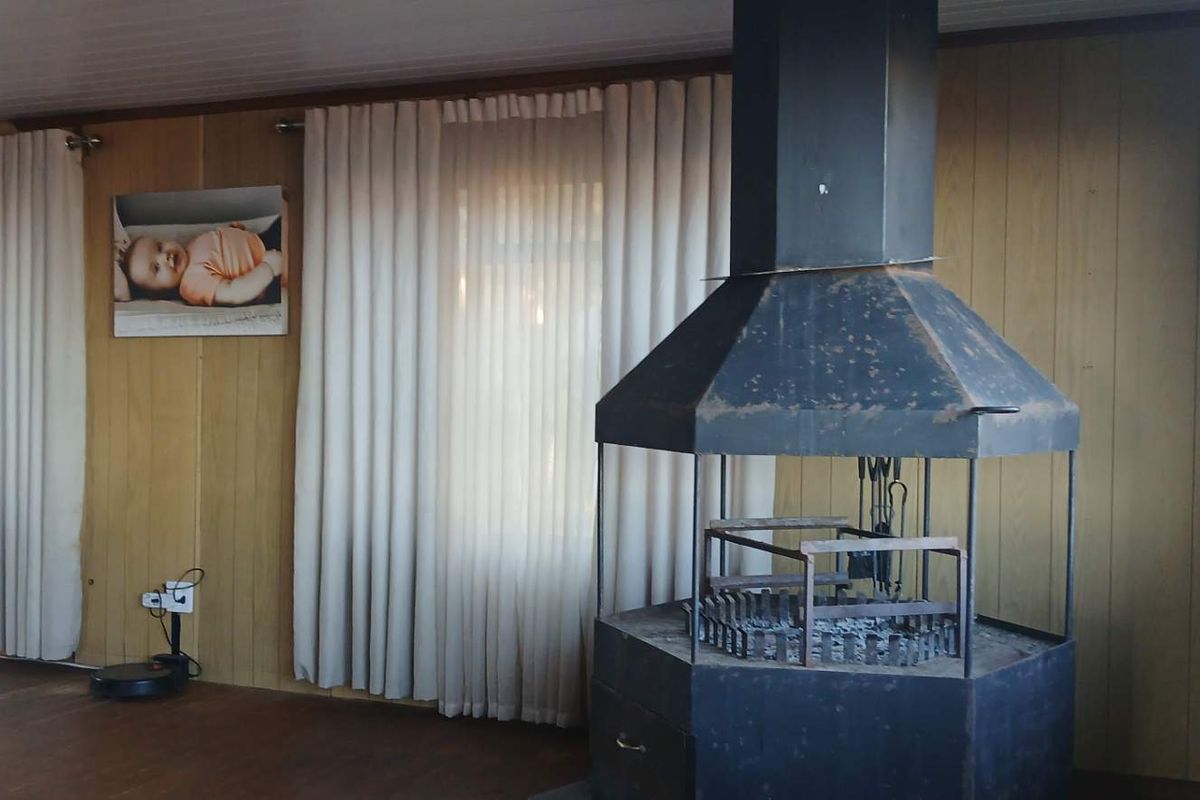 Living area featuring wood paneling, timber flooring, and a prominent central freestanding fireplace.