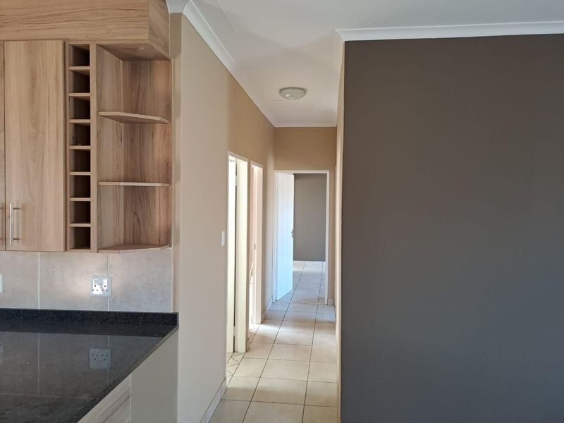 A clean hallway featuring tiled flooring and built-in kitchen cabinetry with granite countertops, leading towards additional rooms in the townhouse.