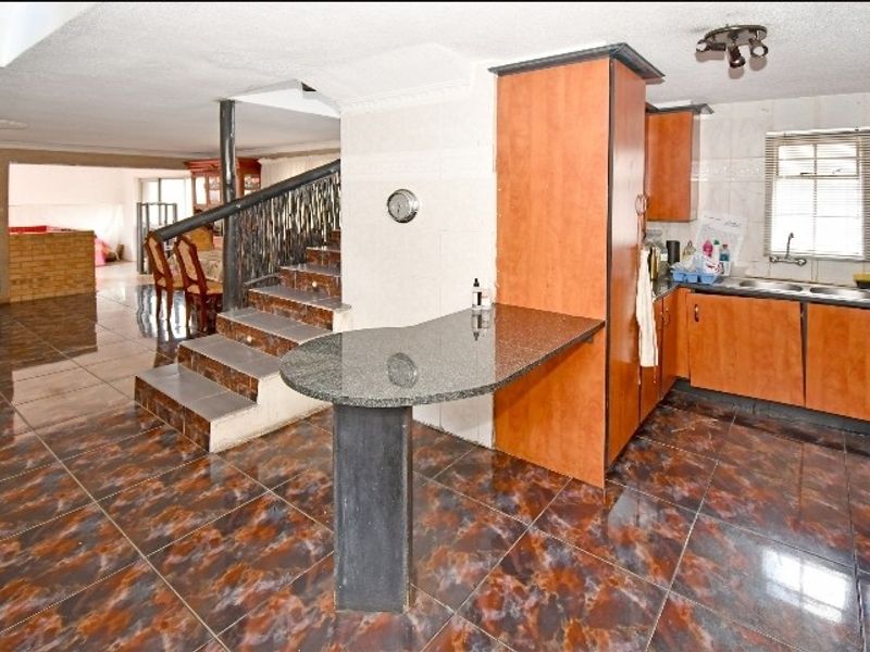 Open plan kitchen area featuring granite breakfast bar, built-in cabinetry, and tiled flooring, adjacent to a staircase leading to the upper level.