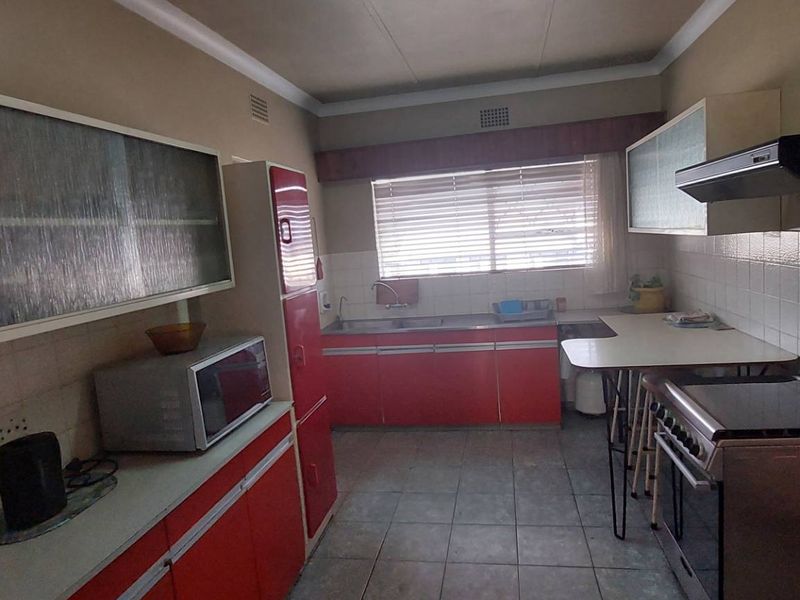 A functional kitchen featuring dated red cabinetry, tiled backsplash, a double sink, and a built-in extractor fan, offering potential for modern renovation.
