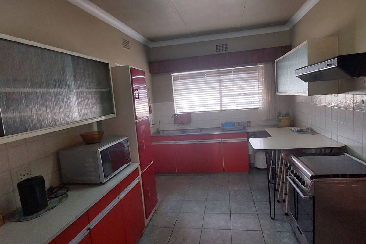 A functional kitchen featuring dated red cabinetry, tiled backsplash, a double sink, and a built-in extractor fan, offering potential for modern renovation.
