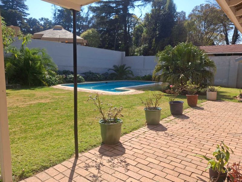 A private backyard featuring a swimming pool, a brick-paved patio area, and a well-maintained lawn enclosed by a perimeter wall.