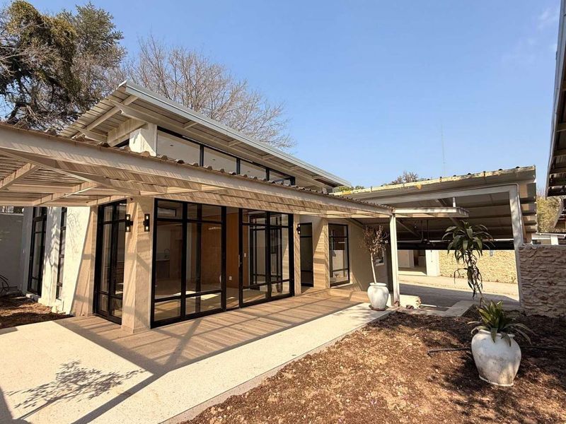 A modern rear exterior view of the townhouse featuring a covered patio, expansive black-framed glass doors, and a well-maintained garden area.