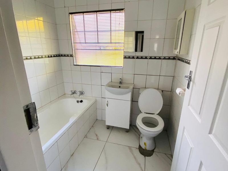 A compact bathroom featuring a bathtub, vanity basin, and toilet with white tiled walls and flooring, requiring minor maintenance and cosmetic updates.