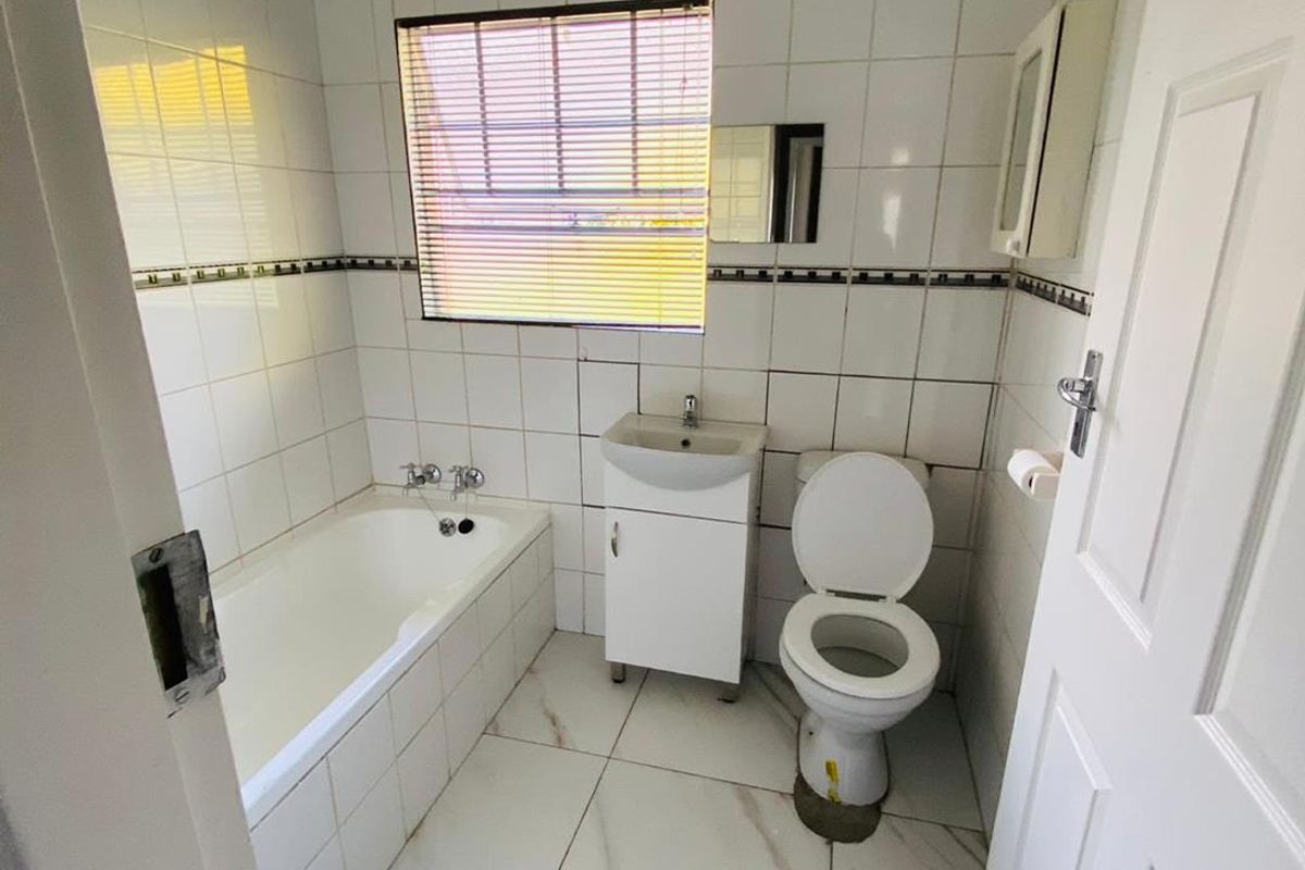 A compact bathroom featuring a bathtub, vanity basin, and toilet with white tiled walls and flooring, requiring minor maintenance and cosmetic updates.