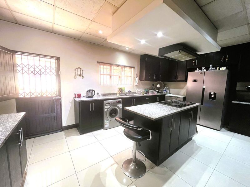 A functional kitchen featuring dark cabinetry, a central island with a built-in hob, granite countertops, and tiled flooring with direct exterior access.