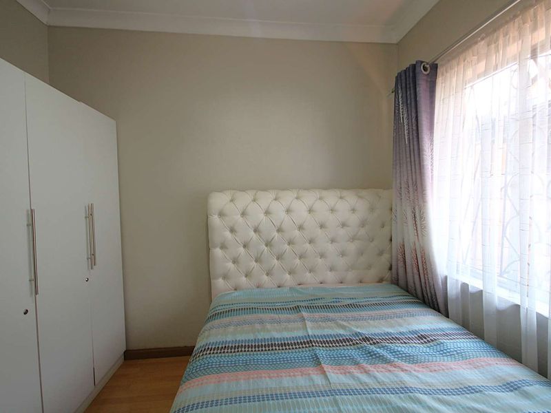 A compact bedroom featuring laminate flooring, a built-in wardrobe, and neutral wall finishes.