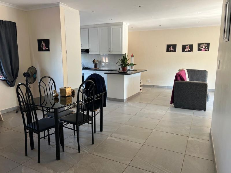 Open-plan living and dining area featuring tiled flooring, recessed lighting, and a functional kitchen with white cabinetry and granite countertops.