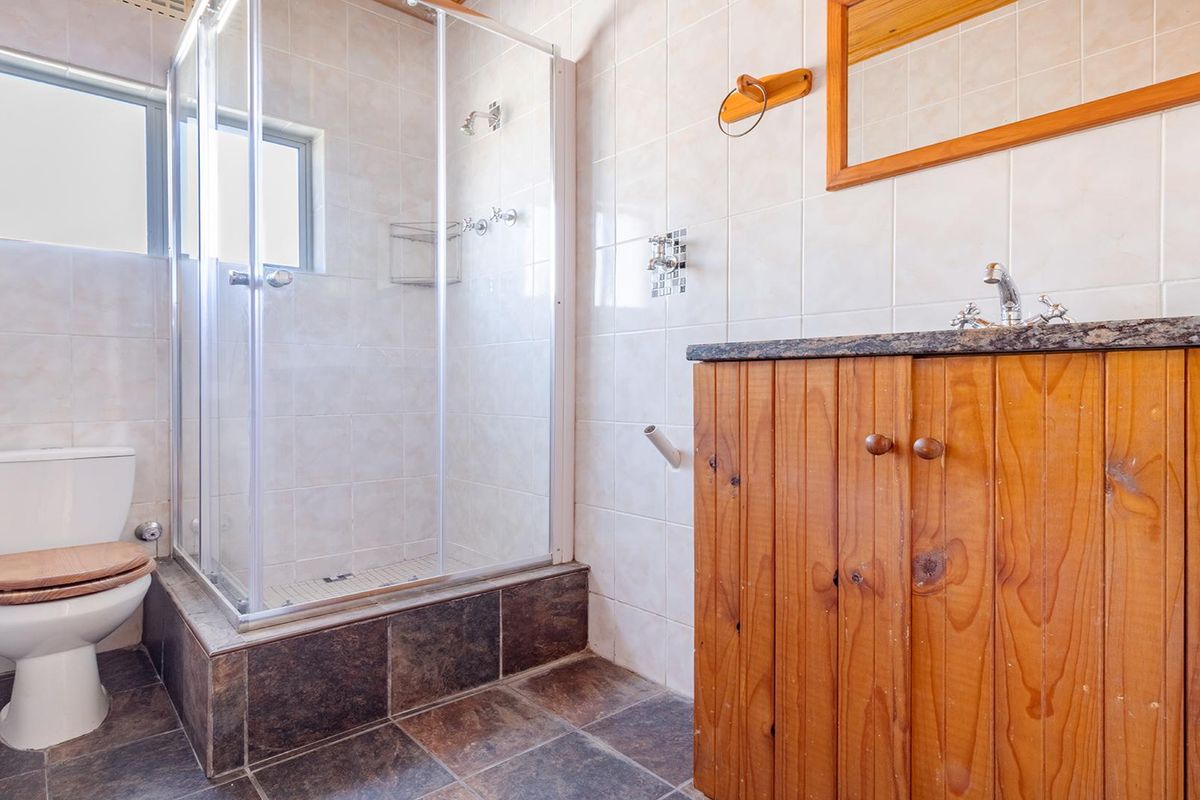 A functional bathroom featuring a glass-enclosed shower, a toilet, and a timber vanity cabinet with a stone countertop.