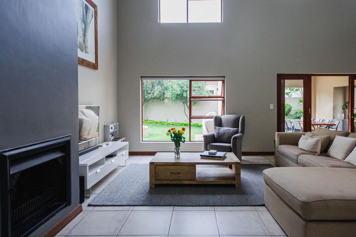 Spacious living room featuring high ceilings, a built-in fireplace, large windows with garden views, and tiled flooring.