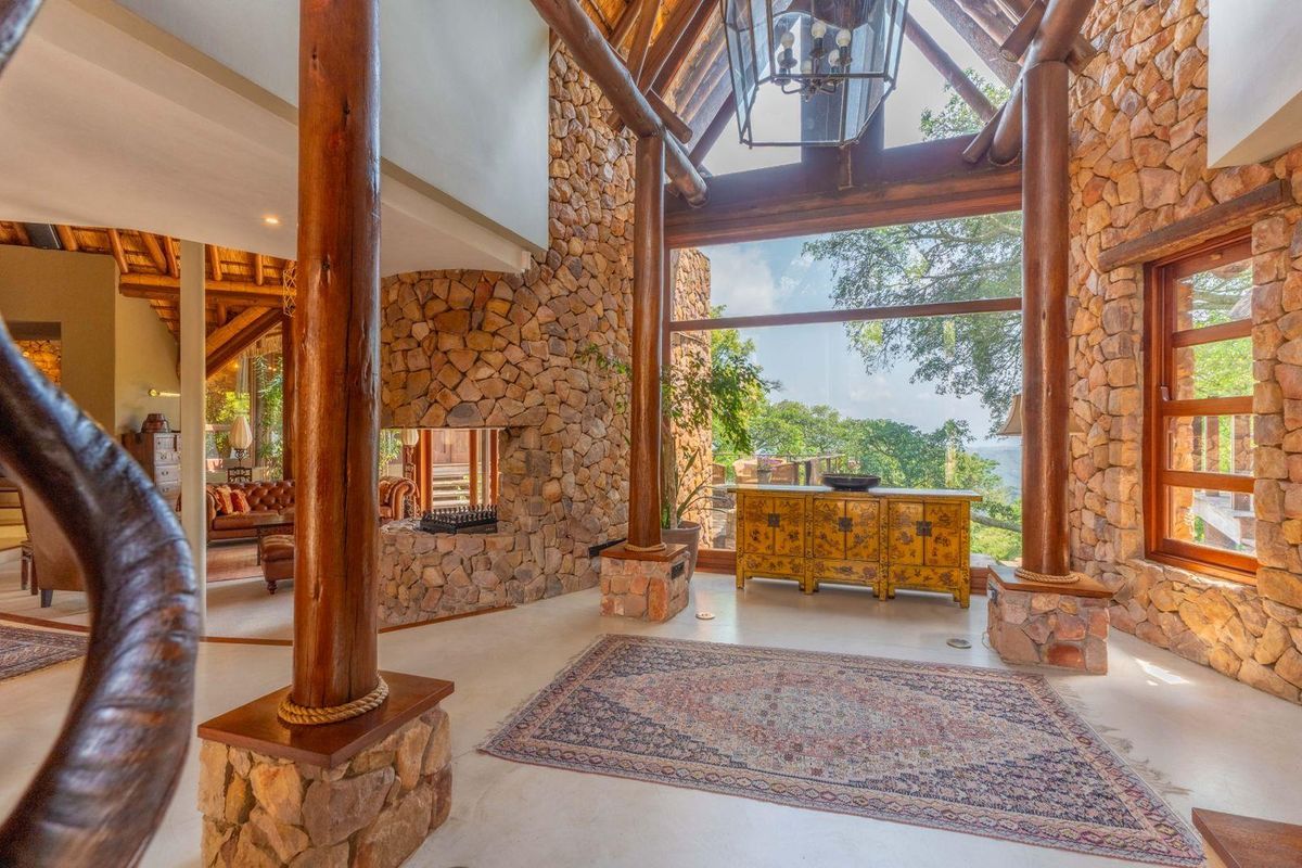 Spacious living area featuring high vaulted timber ceilings, exposed stone walls, large timber support columns, and expansive windows with scenic views.