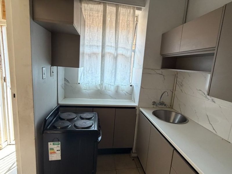 Compact kitchen featuring built-in cabinetry, stone-look backsplash, stainless steel sink, and an electric stove with exposed overhead ducting.