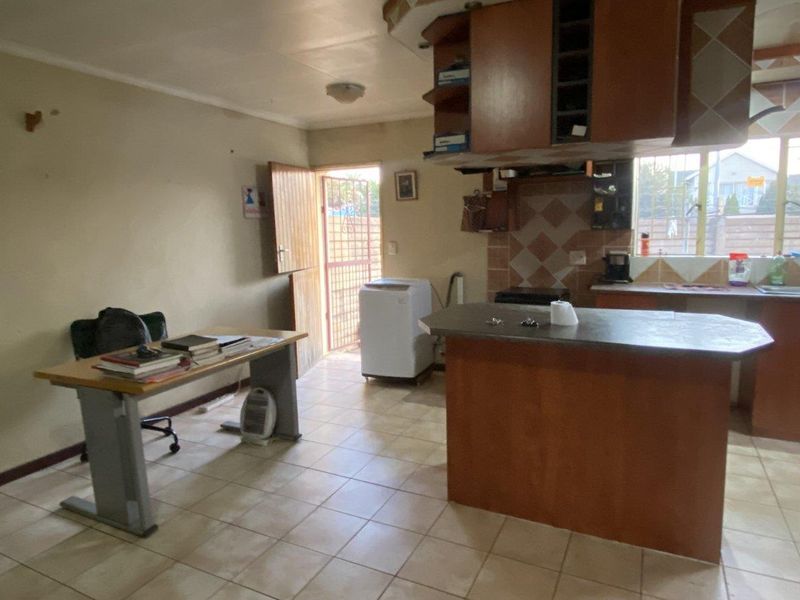 Open-plan kitchen area featuring tiled flooring, built-in cabinetry, and a central island, with direct access to the exterior via a security gate.