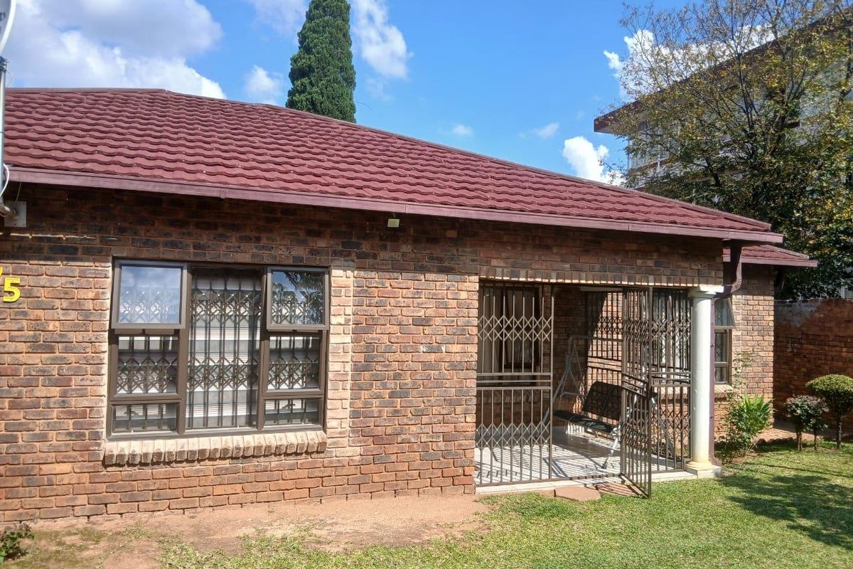 A view of the rear exterior of a brick house featuring a covered patio area with security gates and a small garden.