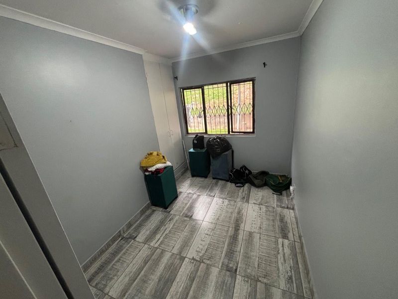 A compact bedroom featuring tiled flooring, built-in cupboards, and security bars on the window, offering a clean and functional space.
