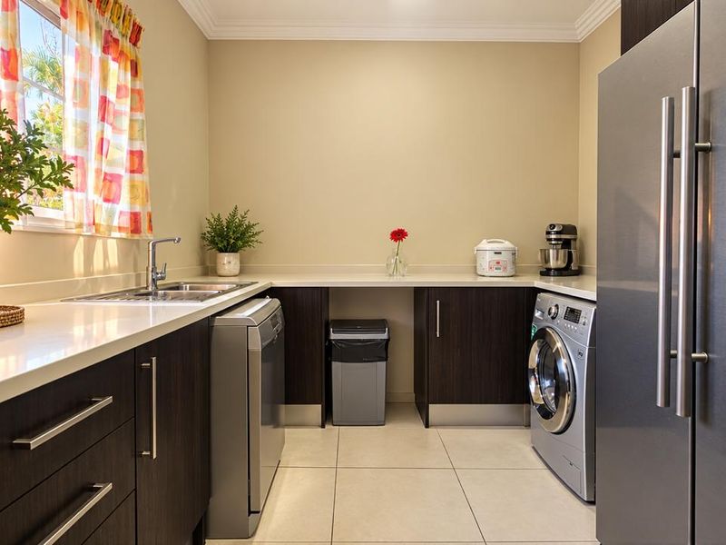 A well-appointed laundry room featuring dark wood cabinetry, stone countertops, a stainless steel sink, and tiled flooring with space for integrated appliances.