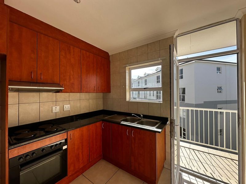 A functional kitchen featuring wood-finish cabinetry, granite countertops, built-in oven and hob, and direct access to an adjacent balcony.