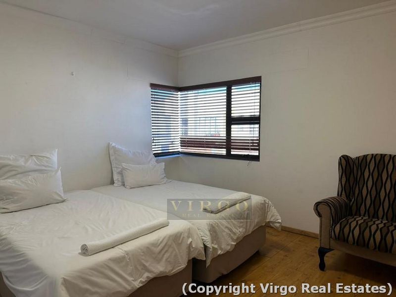 A bedroom featuring timber flooring and a corner window with venetian blinds, requiring minor cosmetic wall repairs.
