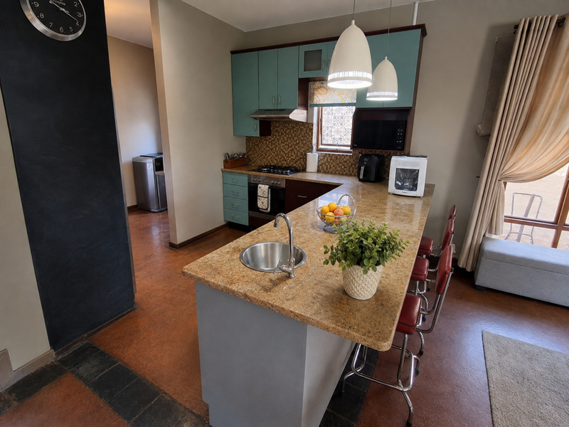A functional kitchen featuring granite countertops, a central island with a sink, gas hob, built-in oven, and teal cabinetry with a tiled backsplash.