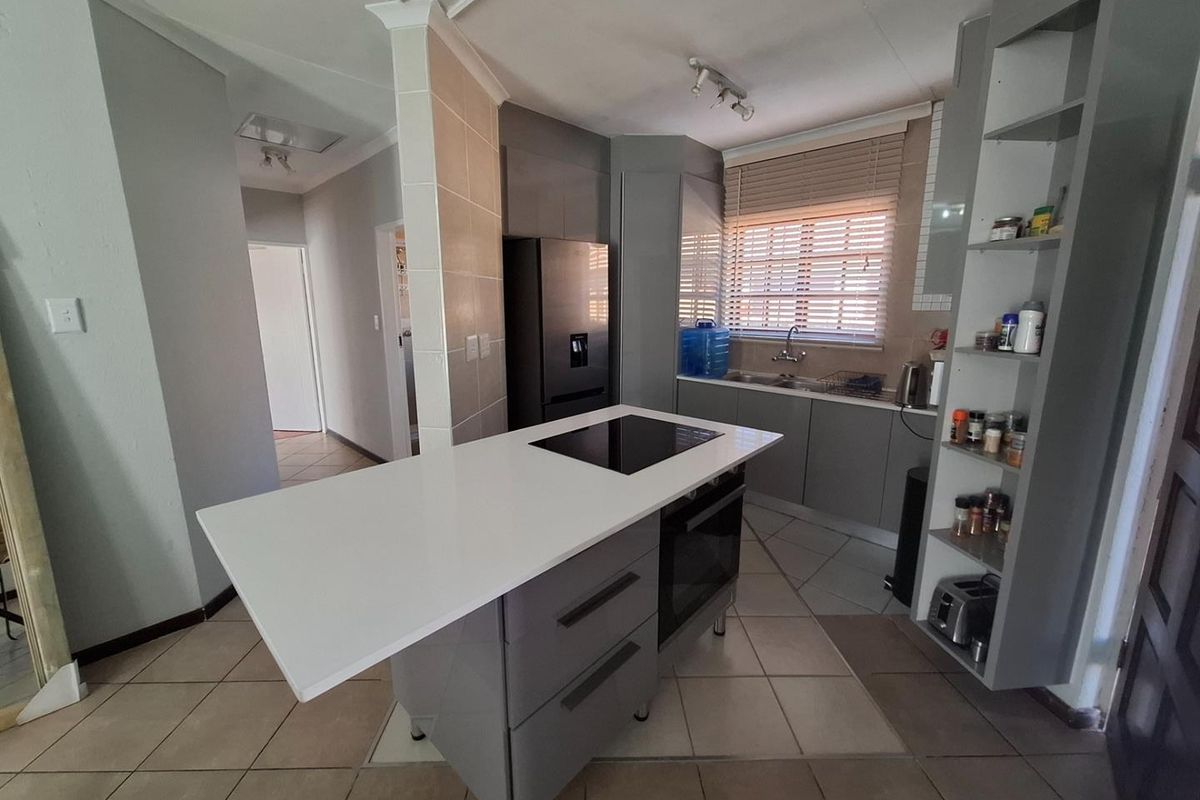 Modern kitchen featuring a central island with a built-in hob and oven, ample cabinetry, open shelving, and tiled flooring.