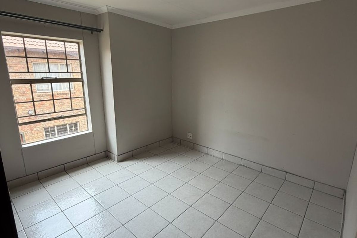 An empty bedroom featuring neutral wall paint, tiled flooring, and a window fitted with security bars.