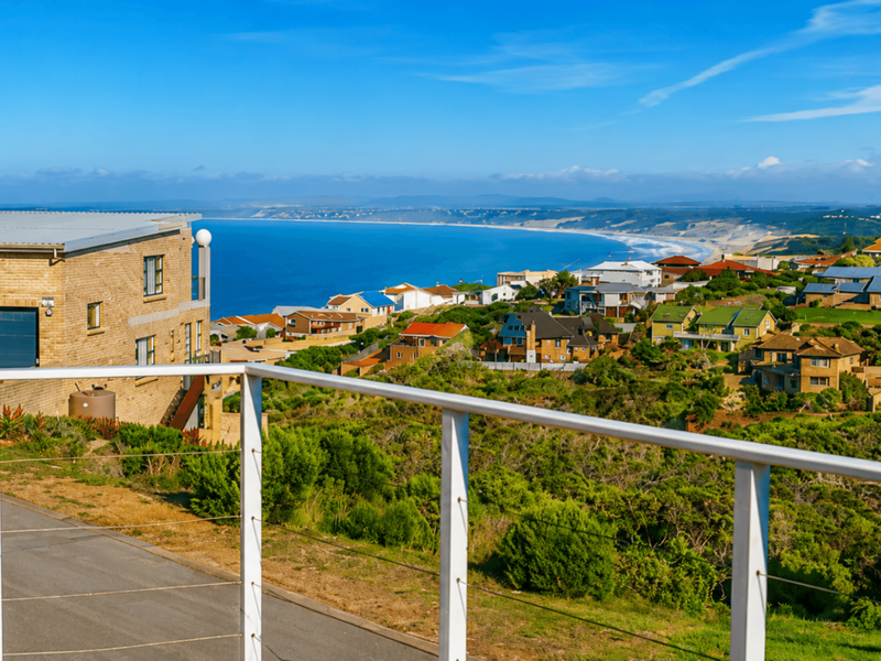 Elevated coastal view overlooking the surrounding residential neighbourhood and coastline, captured from a balcony with a modern white railing.