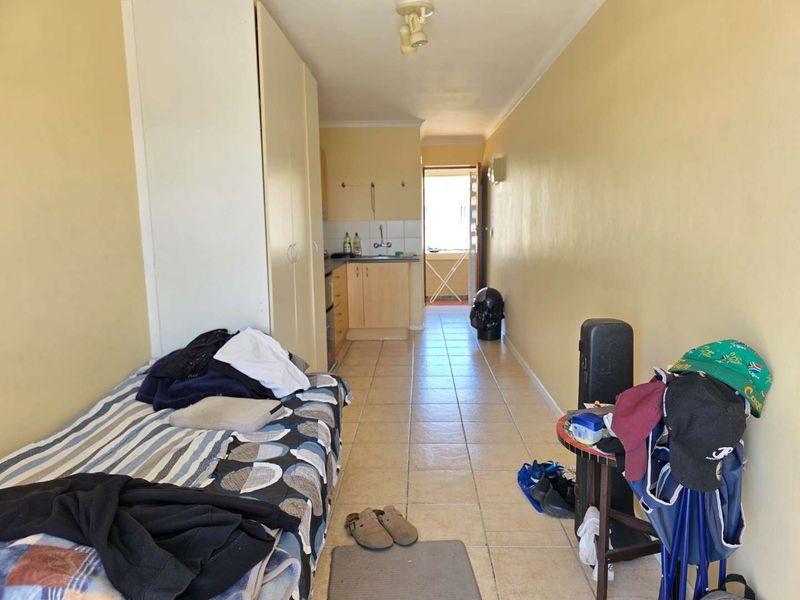 An open-plan studio apartment featuring tiled flooring, built-in cupboards, and a compact kitchenette area with sink and cabinetry.